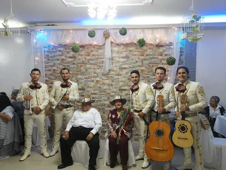 Mariachi juvenil posando junto a una pareja de adultos mayores con sombrero vueltiao en la celebración de su aniversario