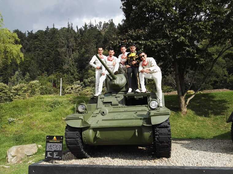 Los cinco integrantes del mariachi juvenil posando sobre un tanque antiguo exhibido en un parque
