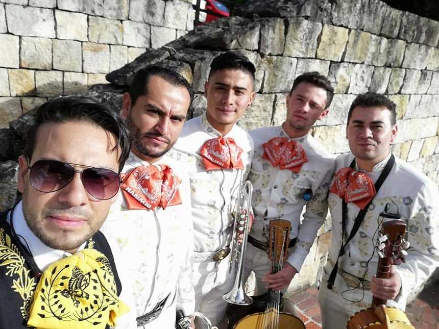 Selfie de los cinco músicos del mariachi con trompeta y vihuelas: cuatro con moño naranja y uno con traje negro y moño amarillo